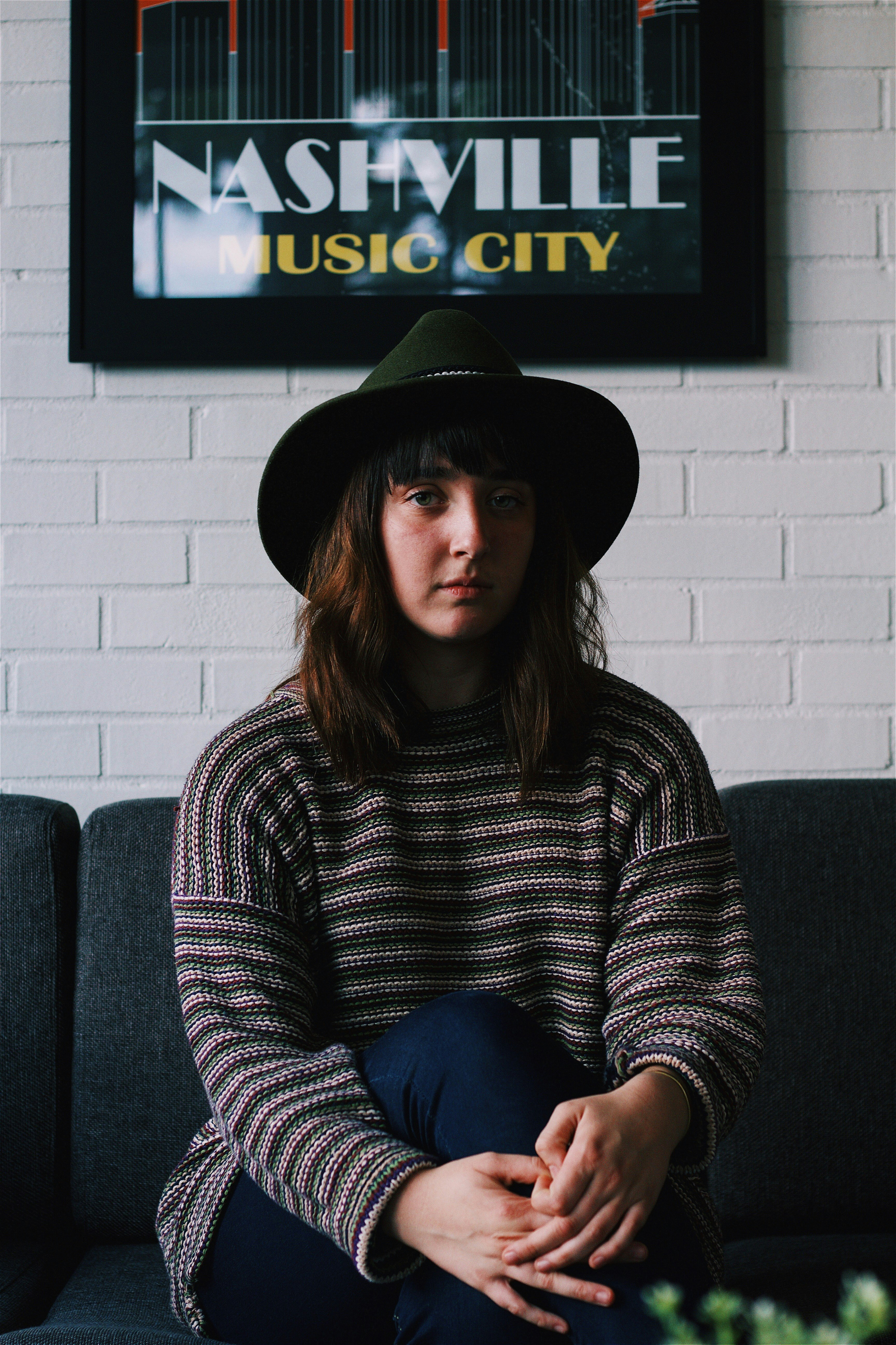 woman sitting on black fabric sofa near Nashville Music City bar mirror